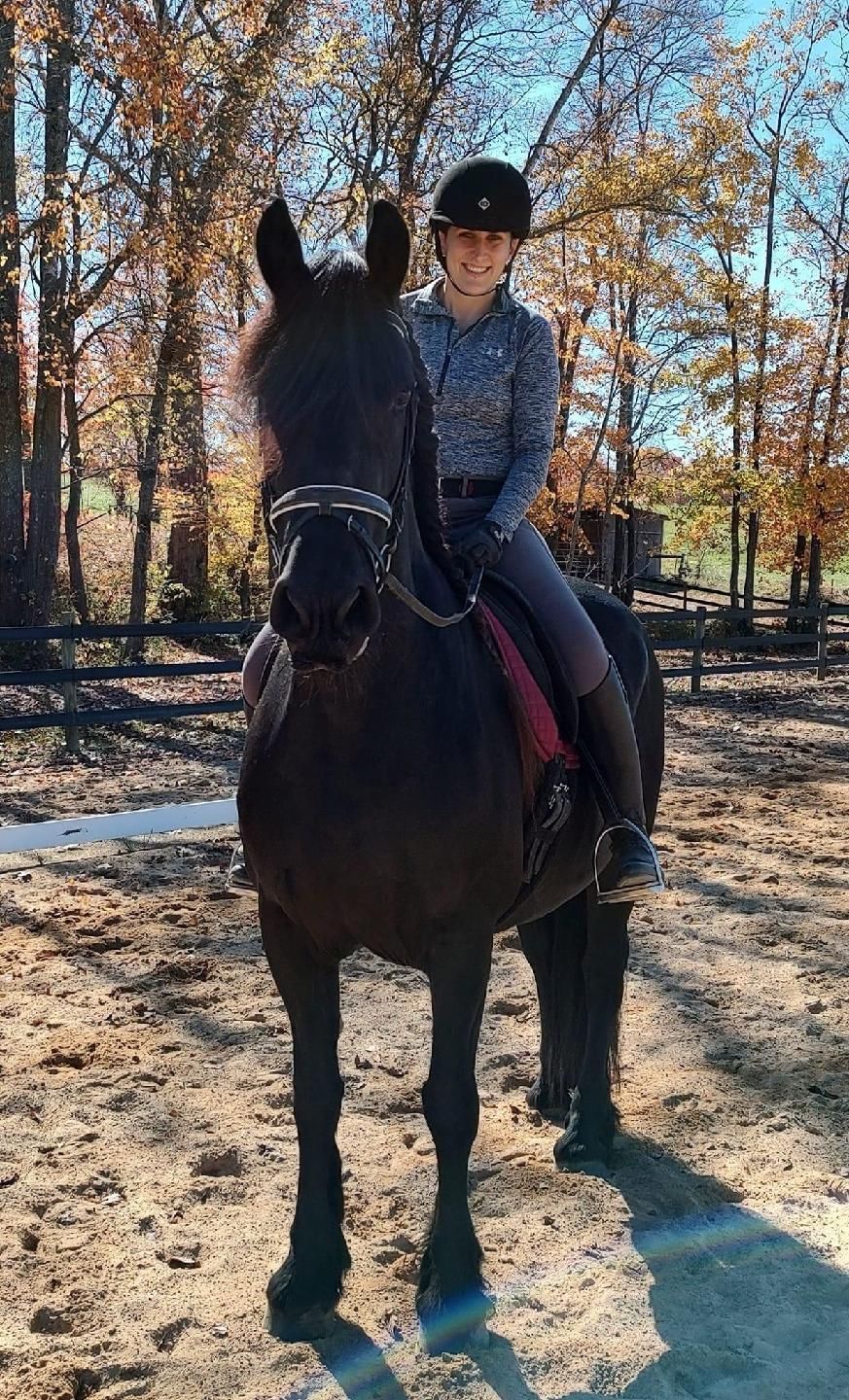 A woman is riding a black horse in a dirt field.