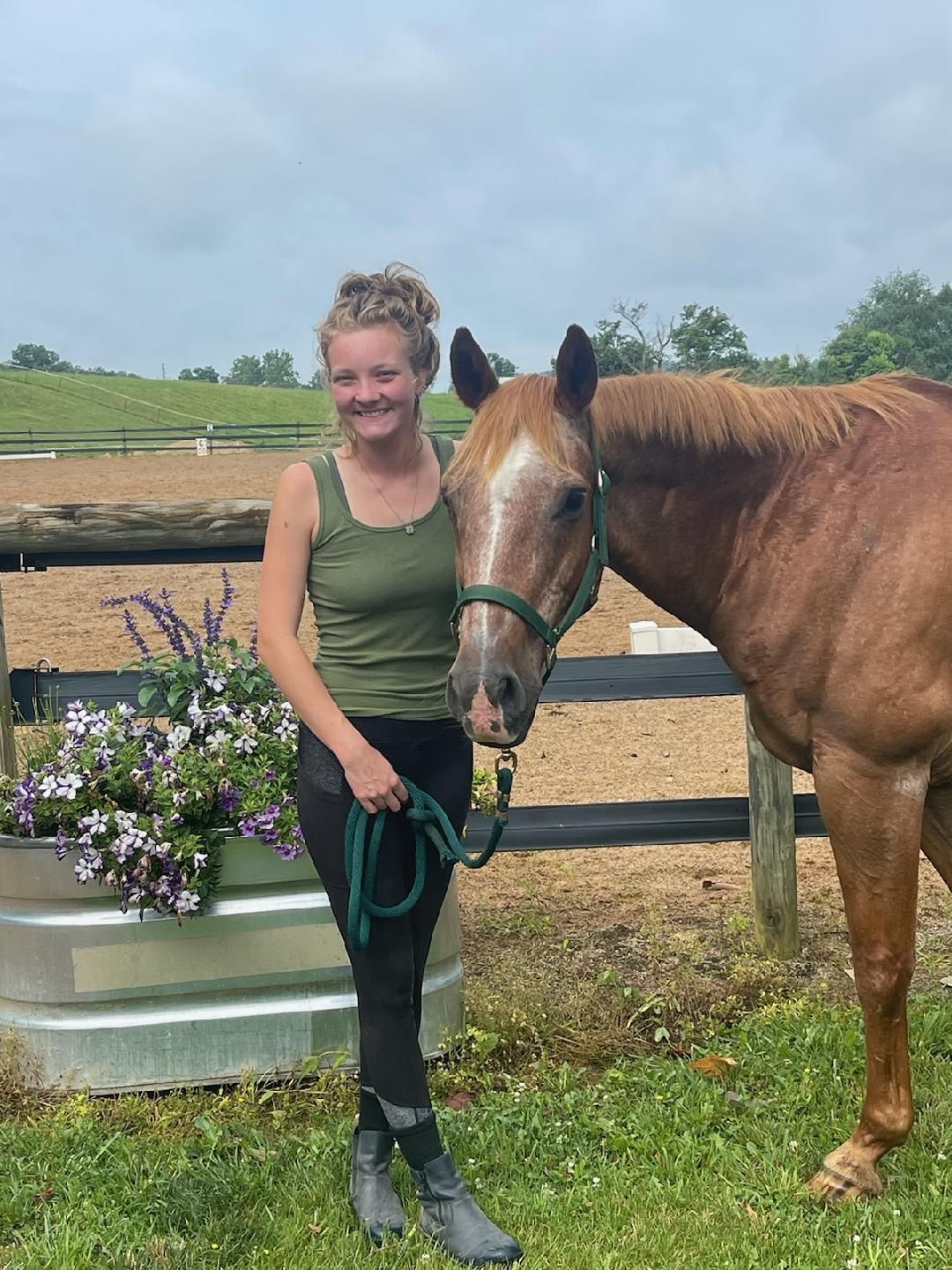 A woman is standing next to a brown horse in a field.