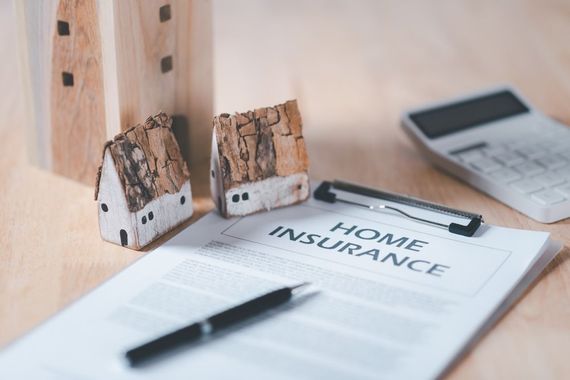Home insurance document on desk with pen, house keys, and a calculator in the background