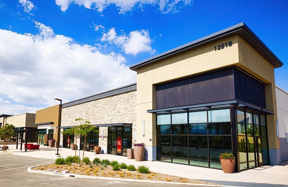 Modern storefronts in a shopping plaza under a blue sky