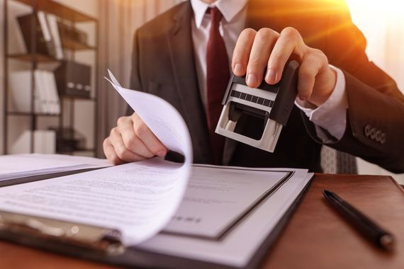 Businessman stamping a document at a desk with papers and a pen in warm light