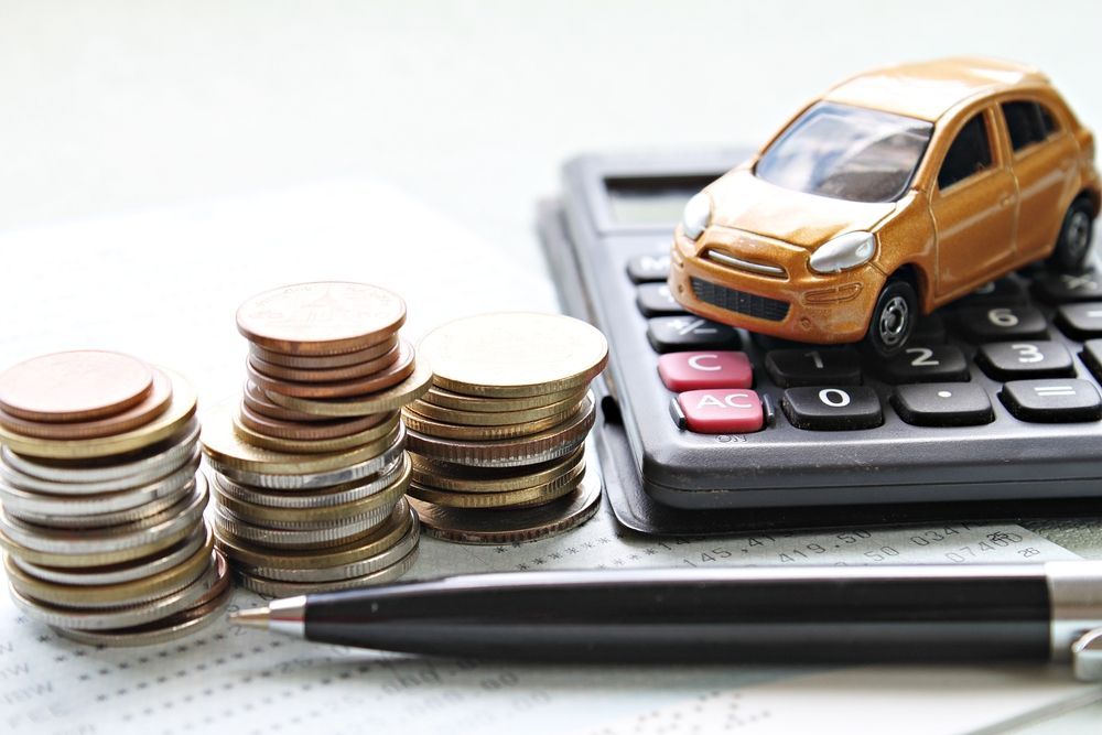 Toy orange car on calculator beside stacked coins and a pen, suggesting vehicle expenses