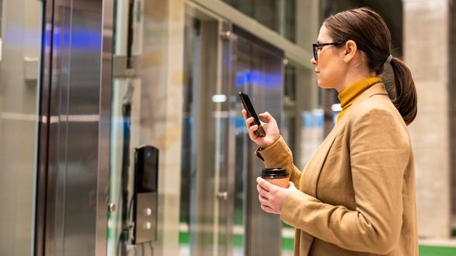 A woman is standing in front of an elevator looking at her cell phone.