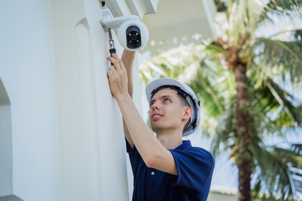 A man is installing a security camera on the side of a building.