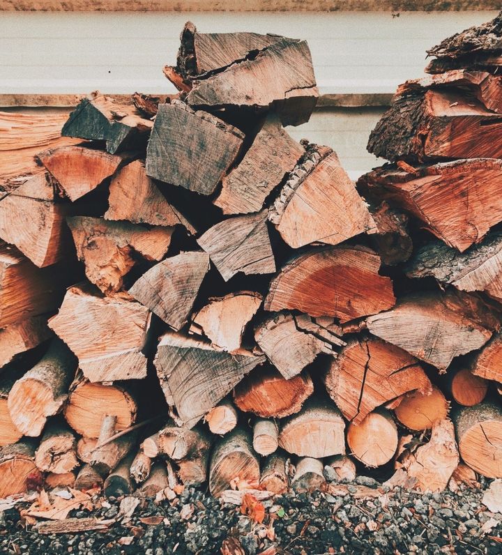 Stacked cut firewood logs against a wall, with gray bark and reddish-brown ends.