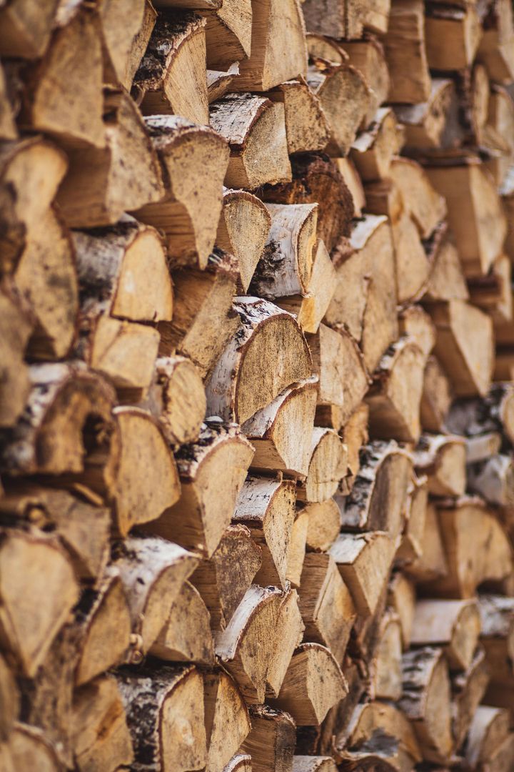Stacked cut firewood logs with rough bark and pale split ends, filling the frame.