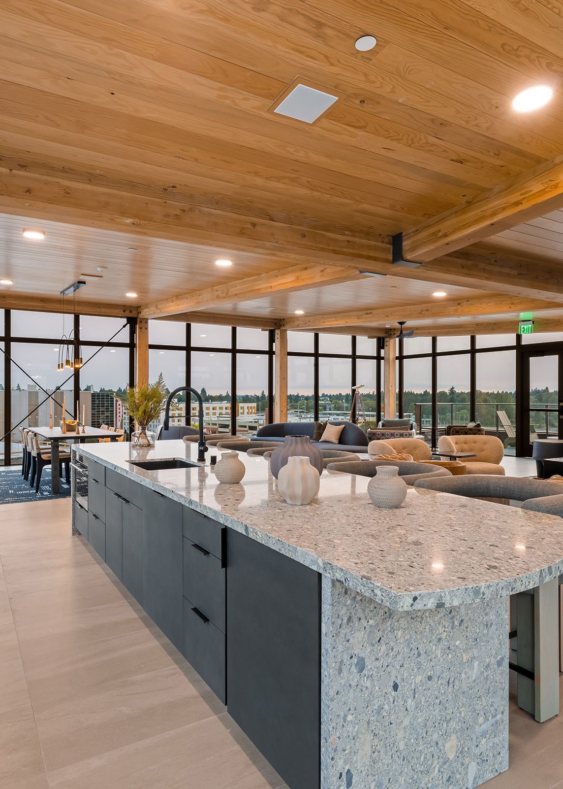 Modern restaurant interior with stone island counter, wood ceiling, and tables by large windows