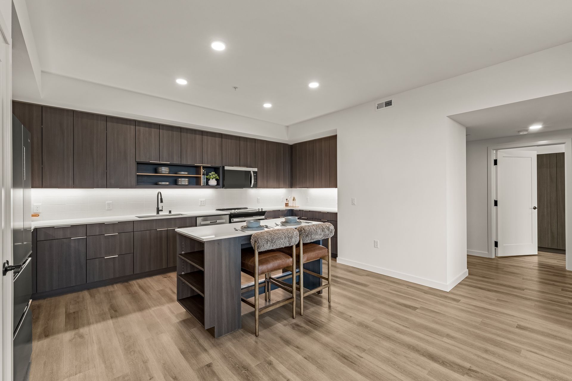 Modern kitchen and dining area with dark cabinets, island seating, and wood floors