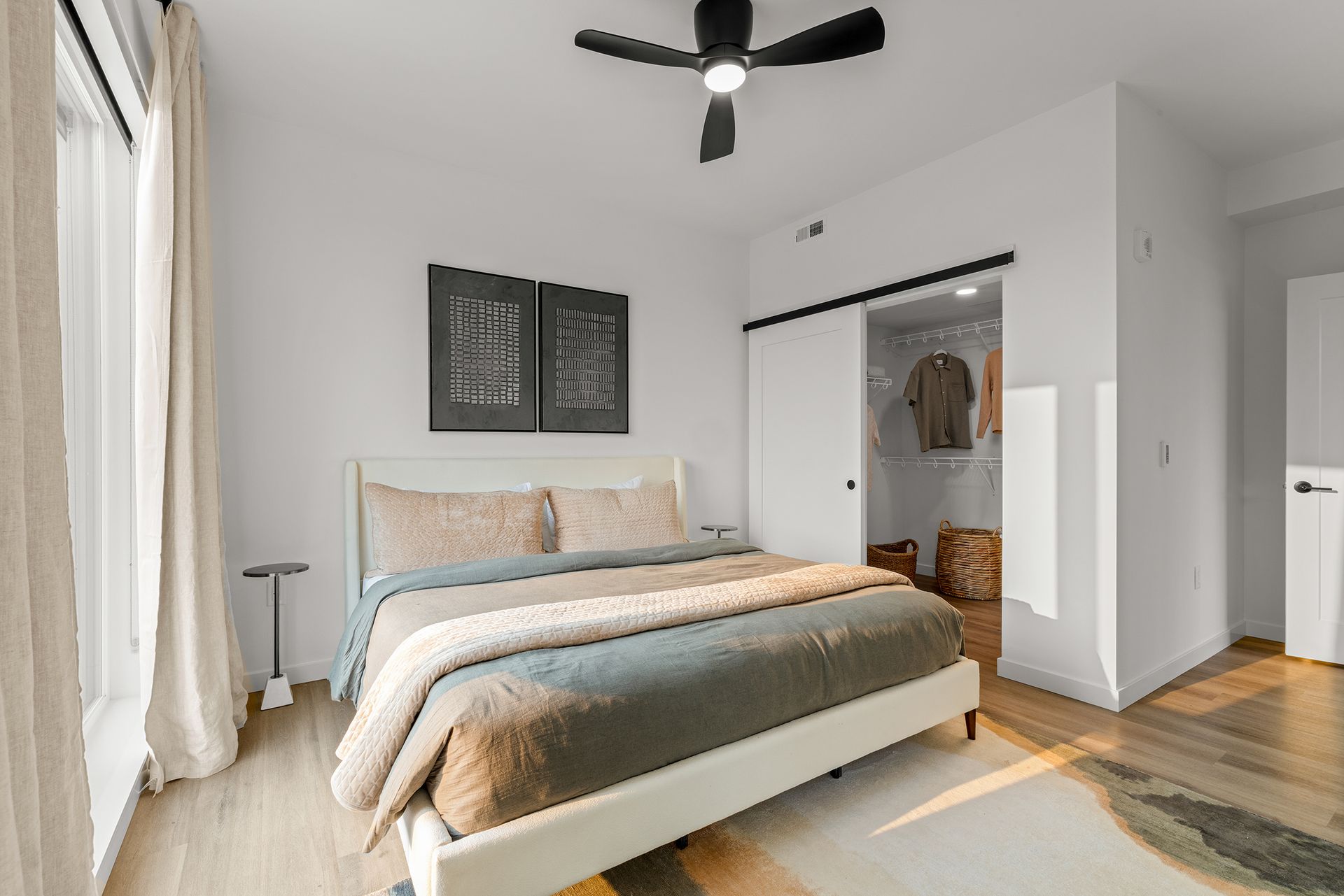 Bright bedroom with a white bed, beige bedding, ceiling fan, and open closet beside a window.