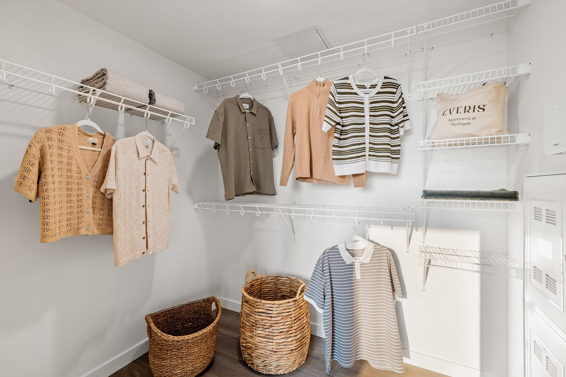 White closet with hanging clothes, woven baskets, and neatly organized shelves.