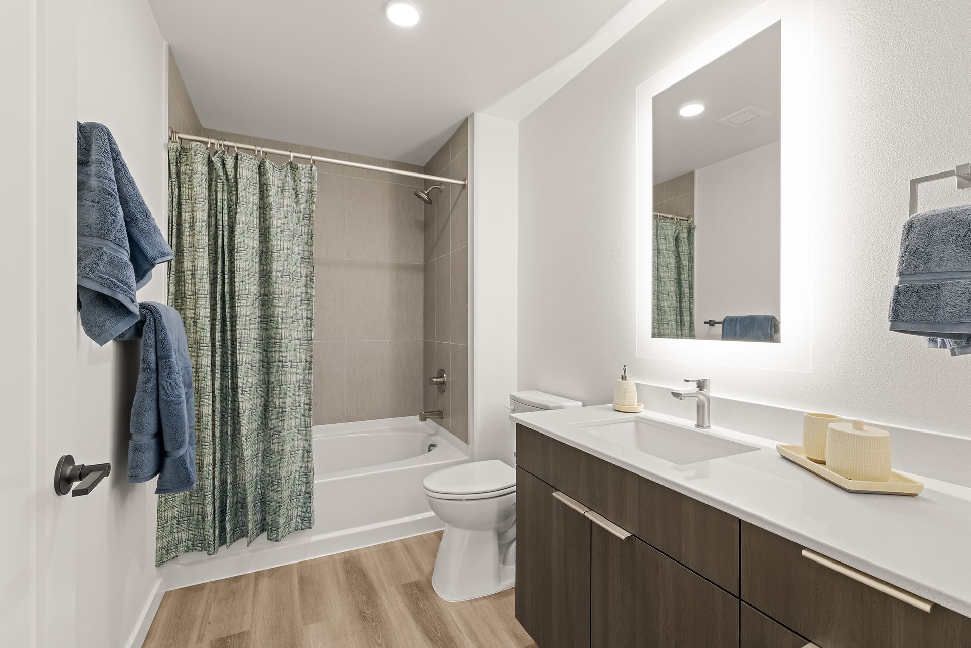 Modern bathroom with bathtub, shower curtain, toilet, and dark wood vanity with sink and mirror.