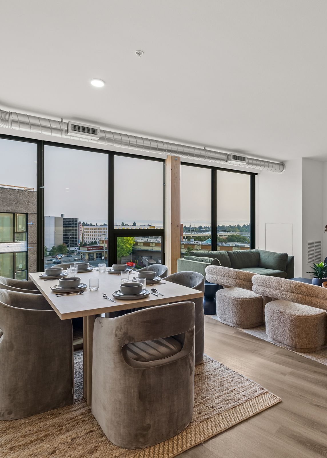 Modern dining area with a wooden table, woven chairs, and floor-to-ceiling windows overlooking a city view
