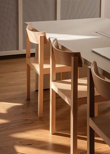 Three light wooden chairs positioned at a modern table, illuminated by sunbeams on a wooden floor.