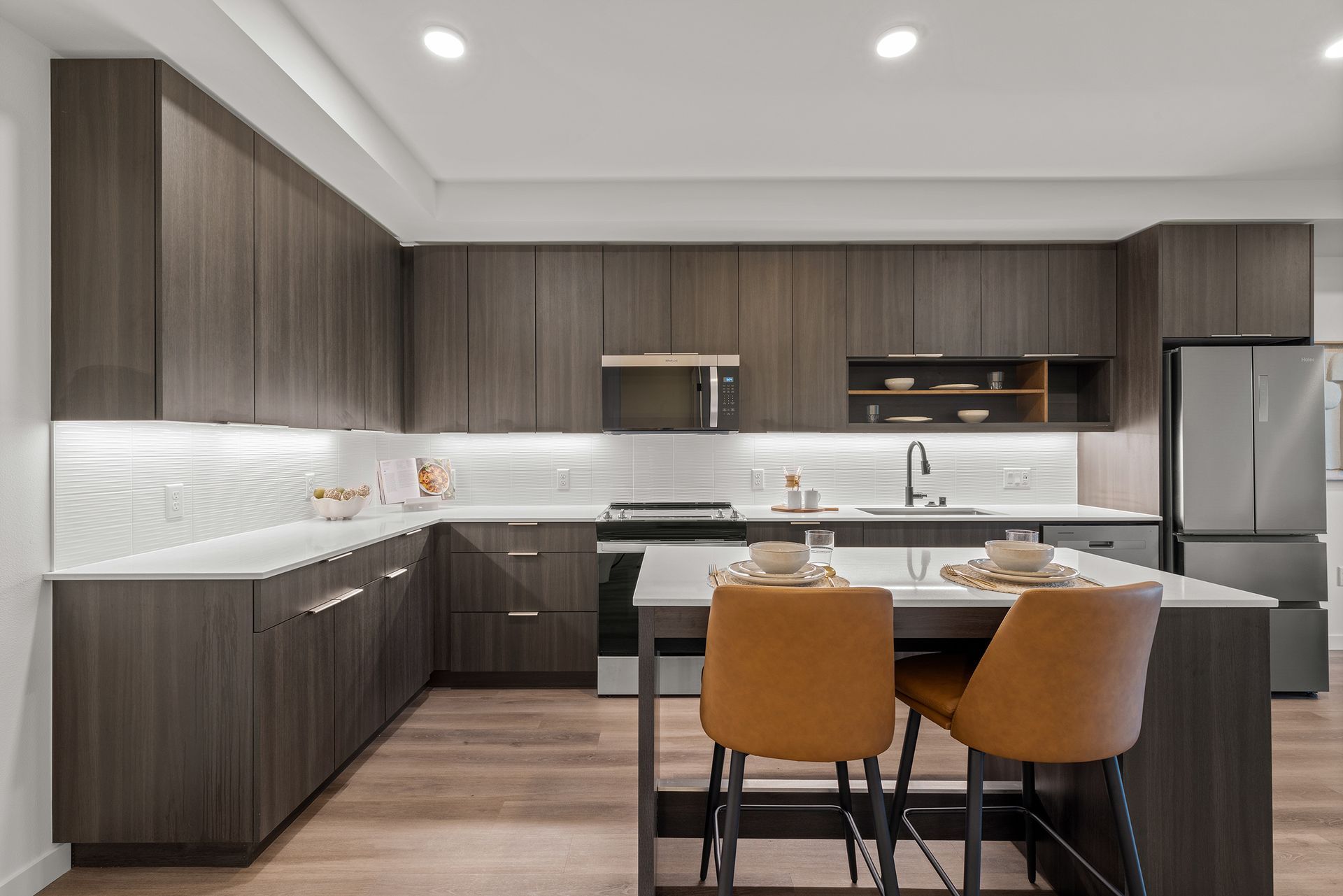 Modern kitchen with wood cabinets, white backsplash, stainless appliances, and two tan bar stools at an island