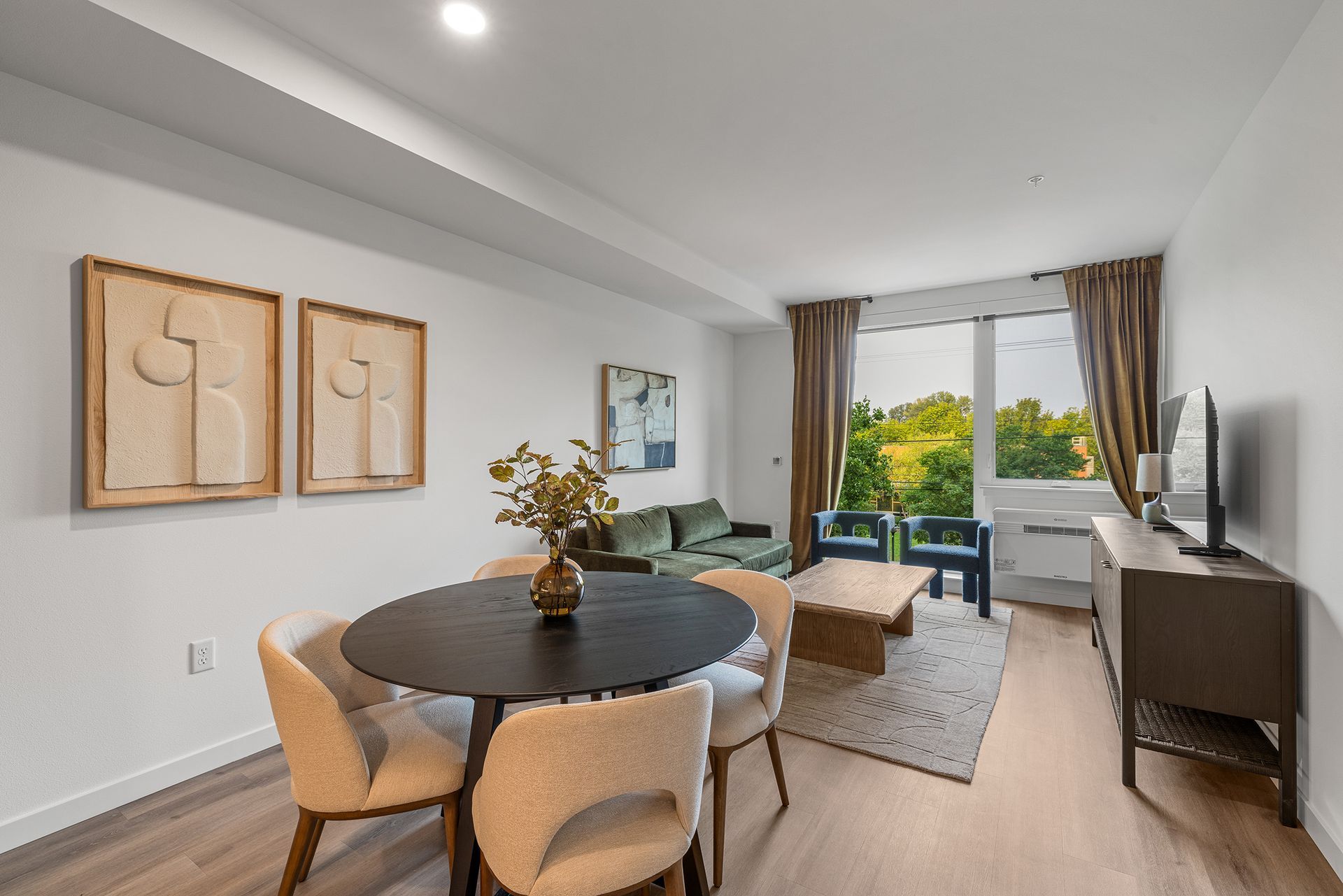 Bright modern living-dining room with round table, chairs, sofa, TV console, and balcony view