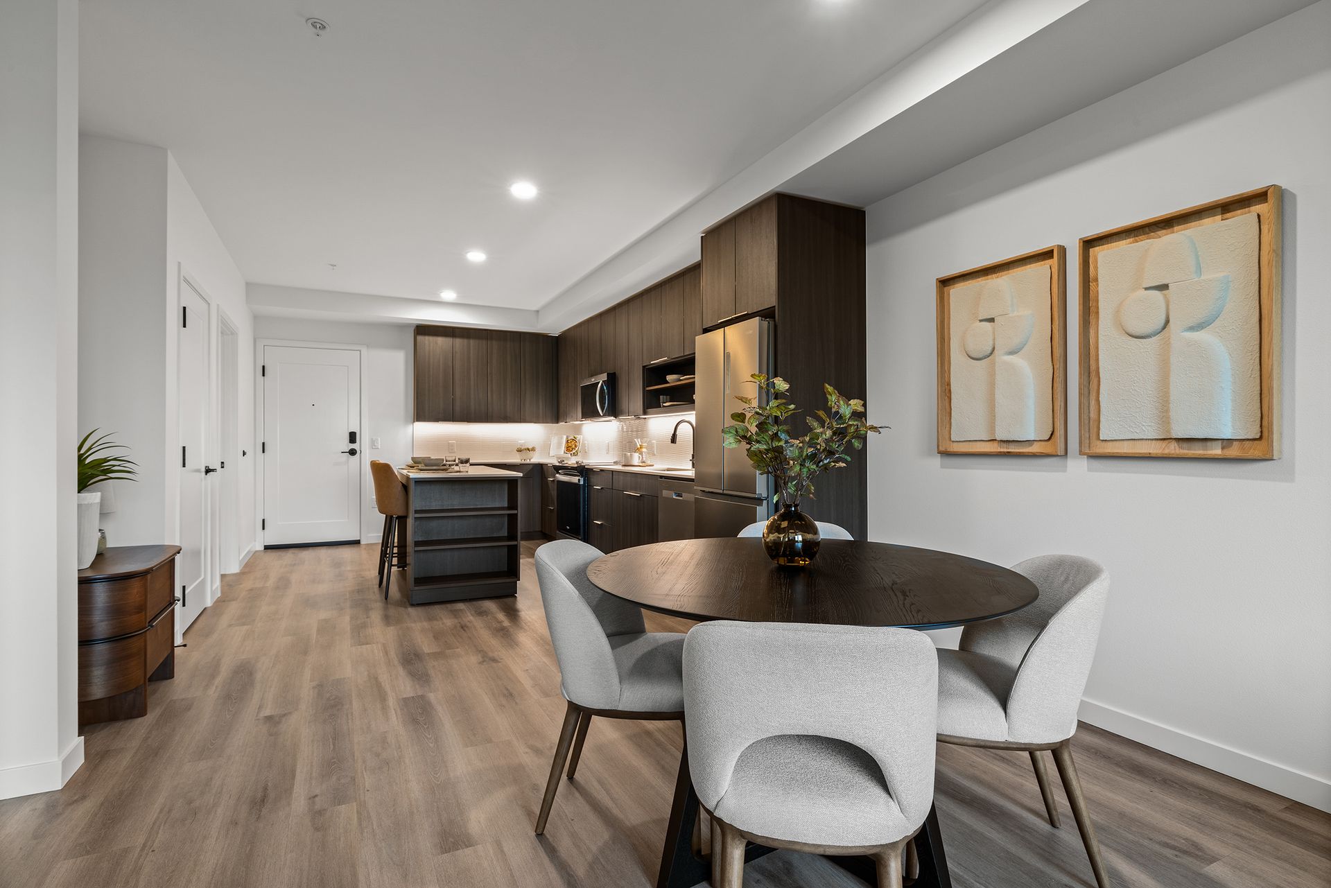 Modern open-plan kitchen and dining area with wood floors, island, round table, and framed wall art