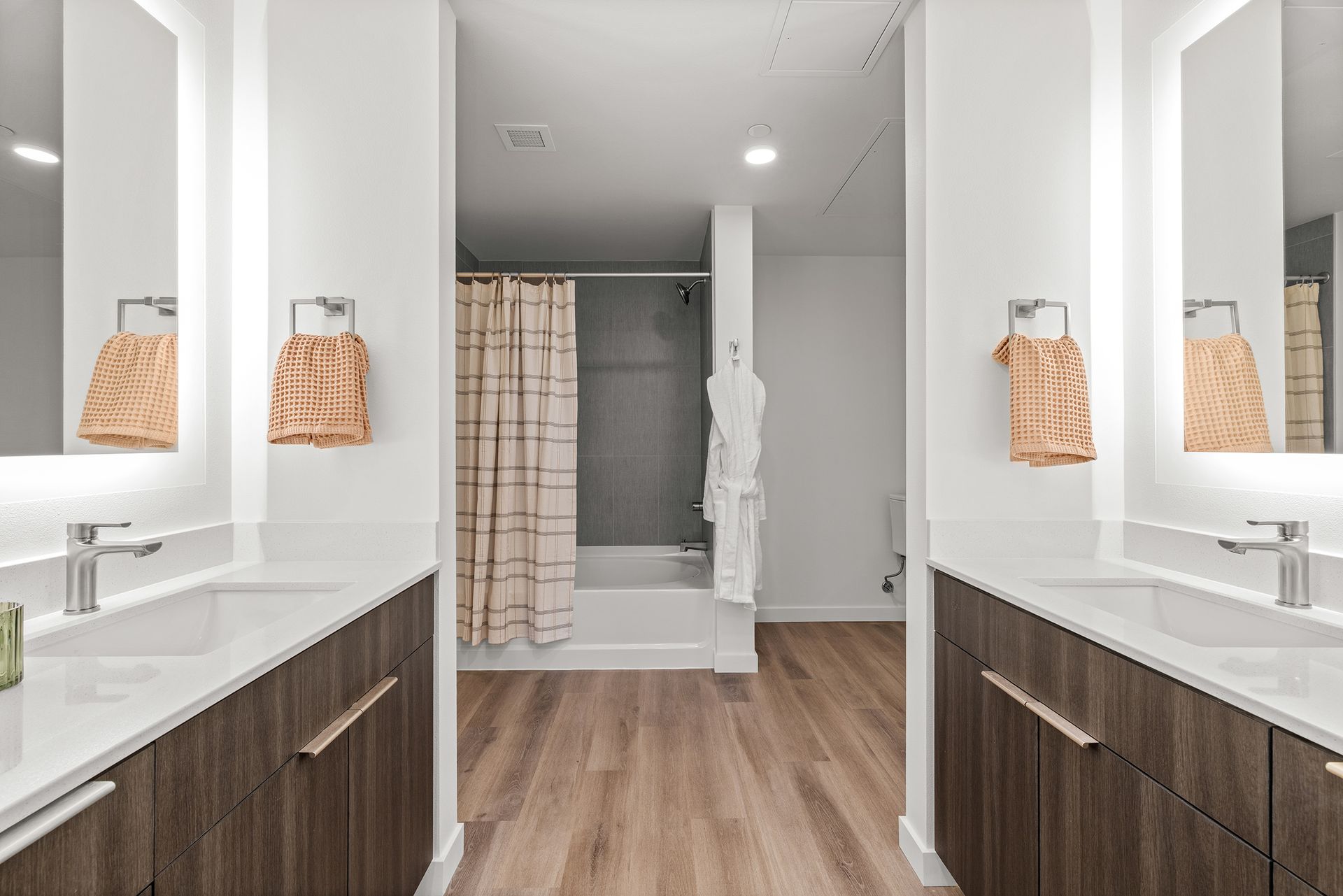Bright modern bathroom with double sinks, wood vanities, and a shower curtain in the center.