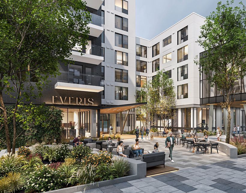 A modern apartment building exterior with a landscaped courtyard, outdoor seating, and people socializing.