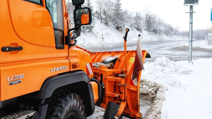 Orange snowplow clearing a snowy roadside in winter
