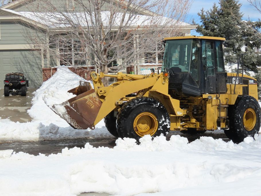 Yellow front loader clearing snow on a residential street in front of a house