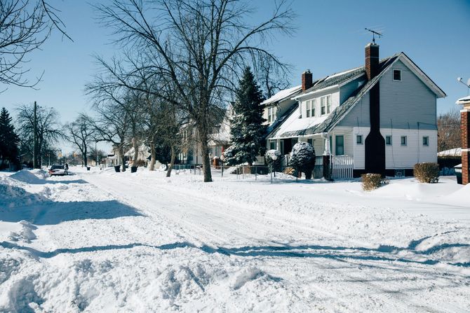 Snow-covered street with white houses and bare trees on a bright winter day