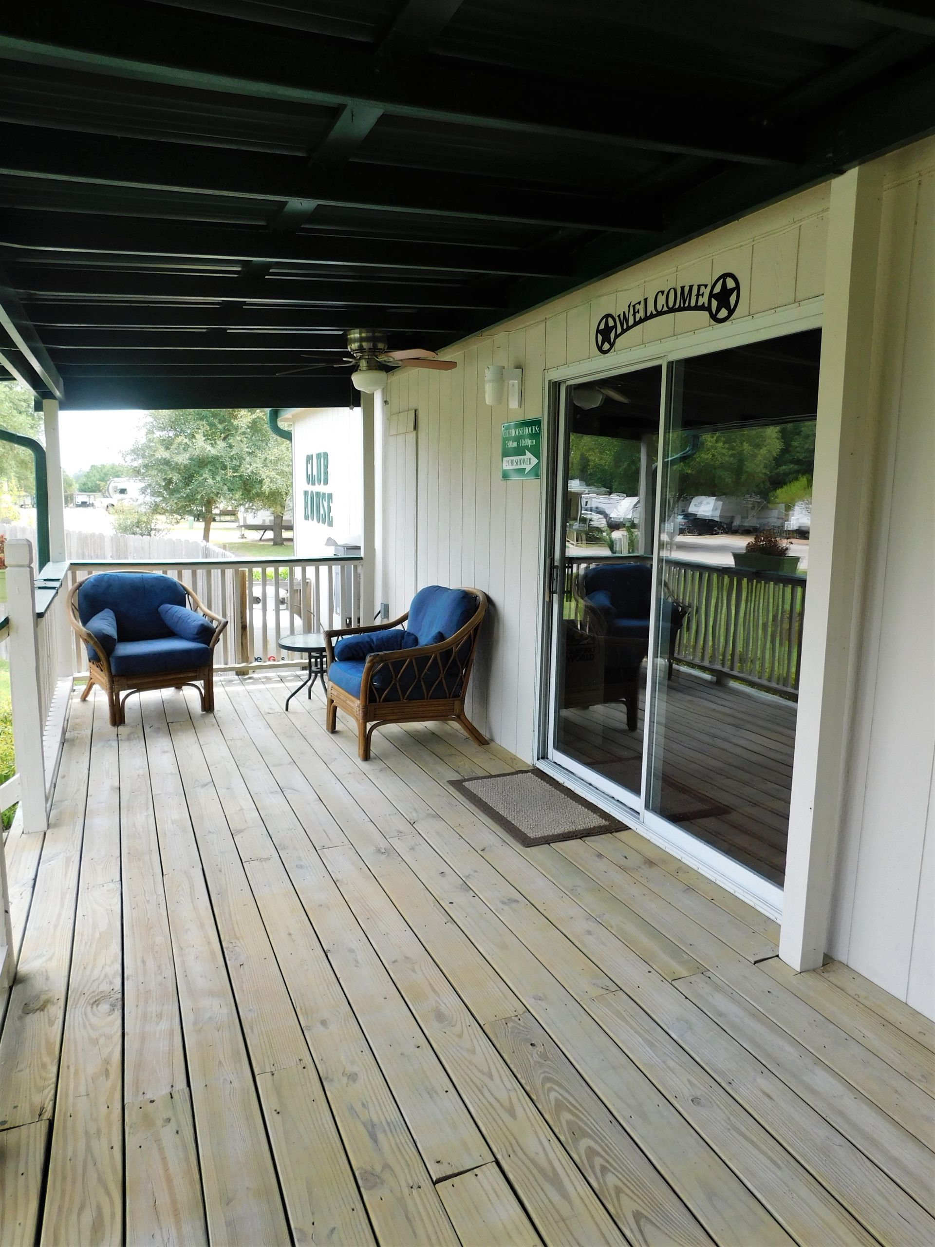 Wooden porch with two blue armchairs, a small table, and sliding glass doors.