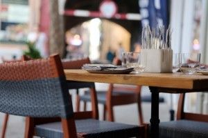 Wooden table set for dining, outdoor restaurant setting. Woven chairs, glasses, silverware.