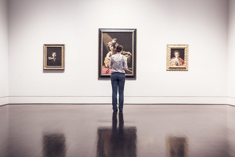 Woman in museum gallery viewing paintings. Bright room with dark, glossy floor.