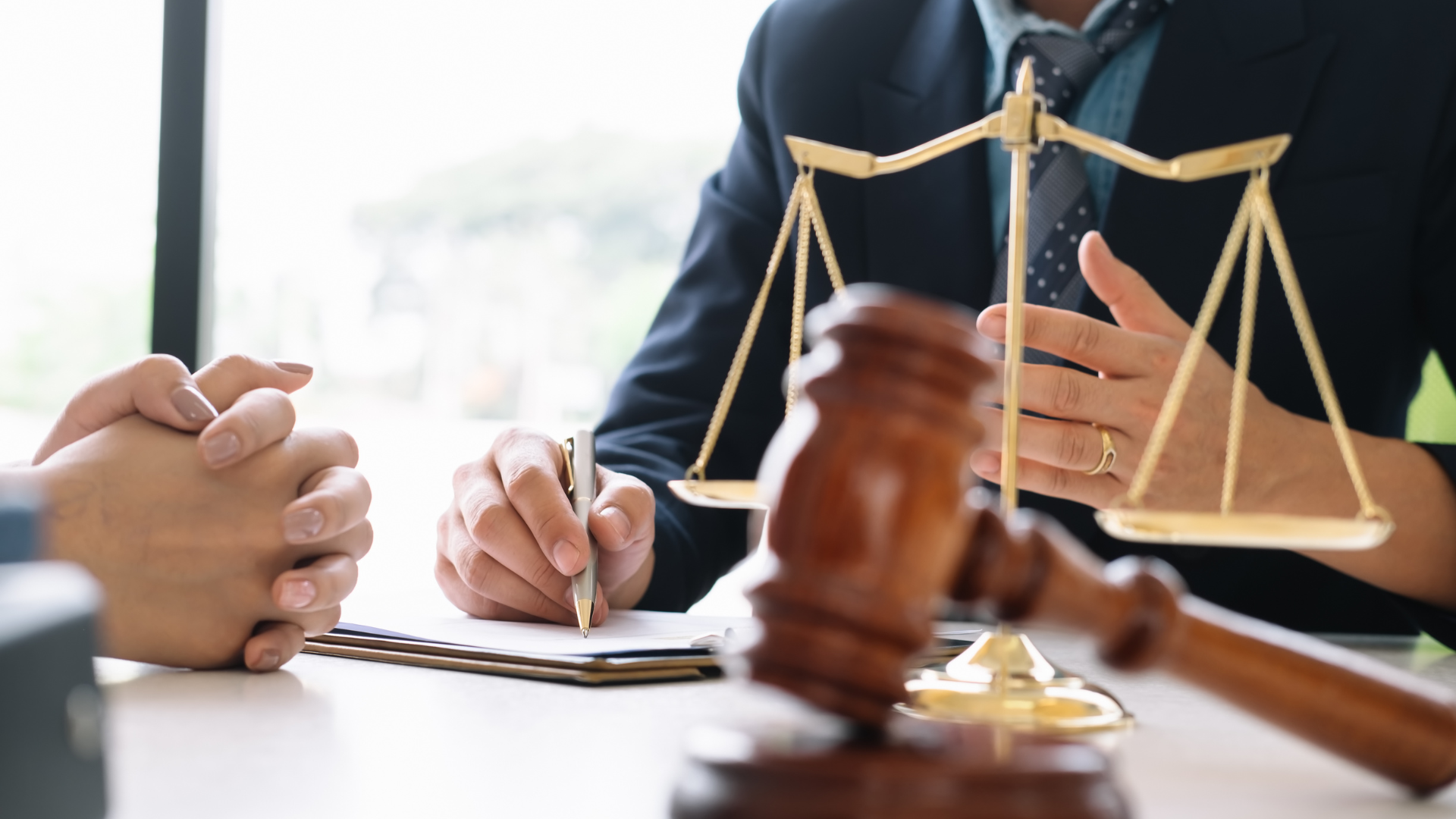 Lawyer advising a client, scales of justice and gavel on desk.