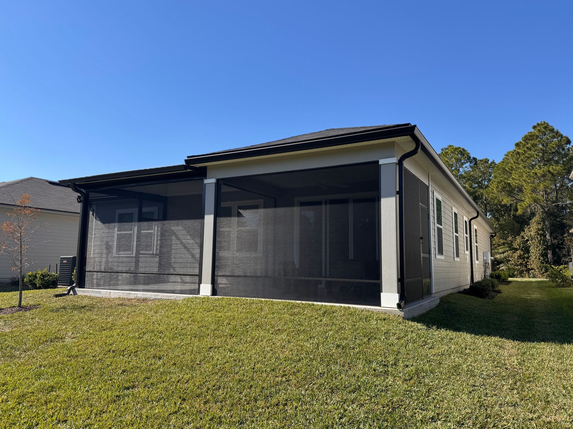 Single-story house with black screened patio and grassy yard under a clear blue sky