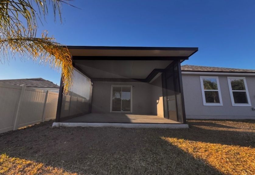 Backyard view of a small covered patio with a window and gravel yard at sunset