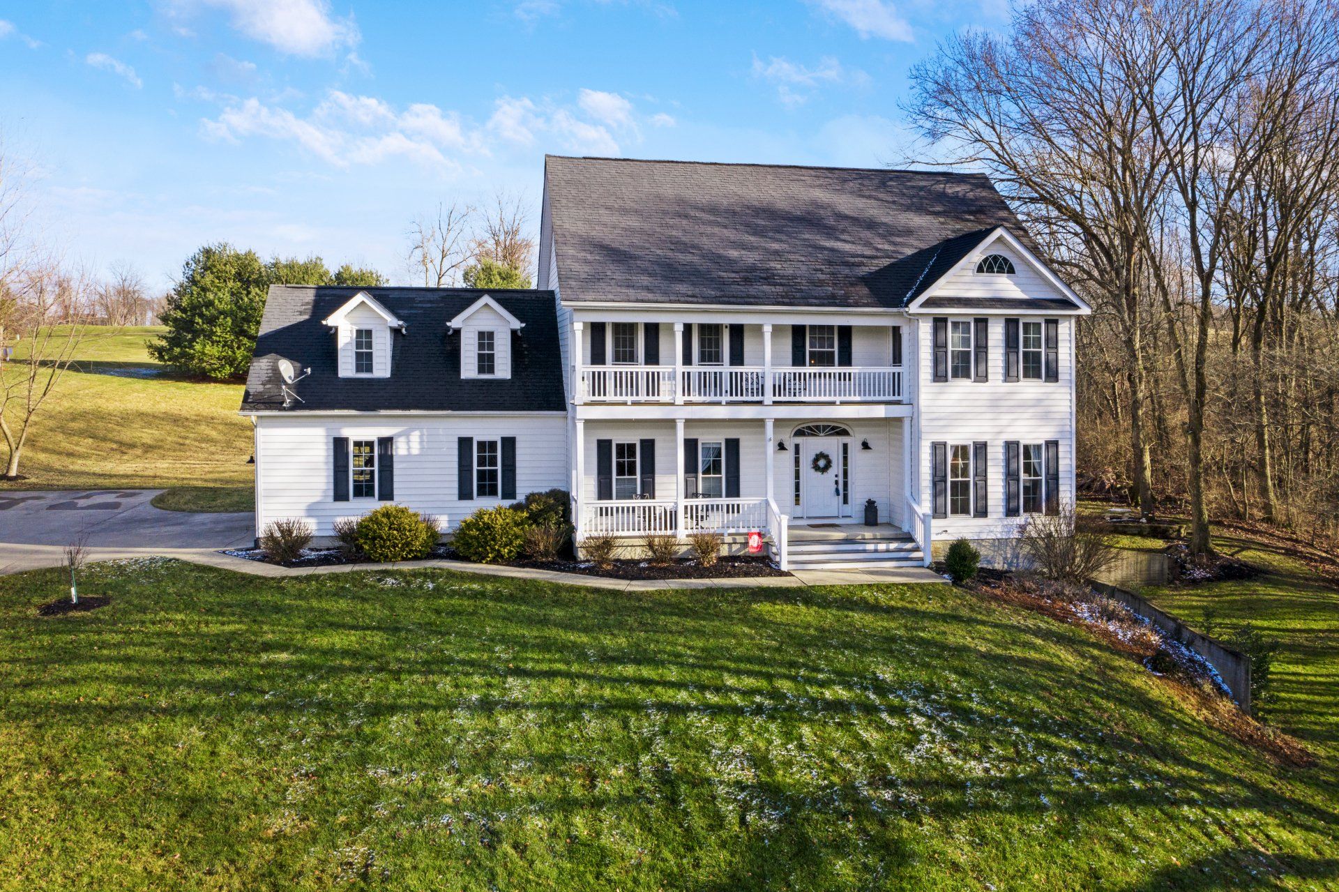 A large white house with black shutters sits in the middle of a lush green field