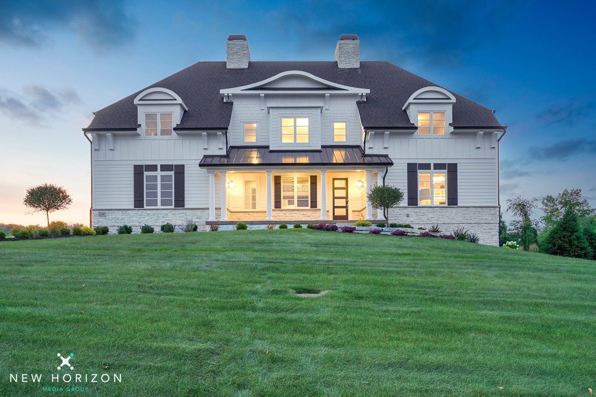 A large white house with black shutters sits on top of a lush green field