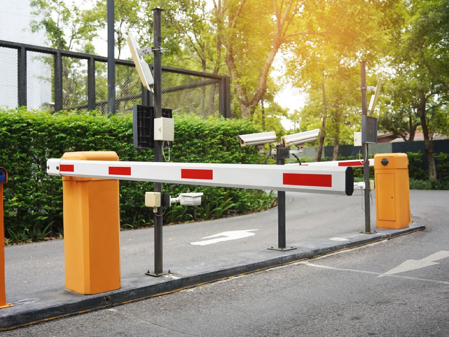Parking barrier with orange and white arm, cameras, and gatehouse.