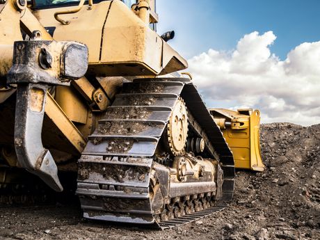 Yellow bulldozer, close-up of tracks, working on a construction site under a blue sky.
