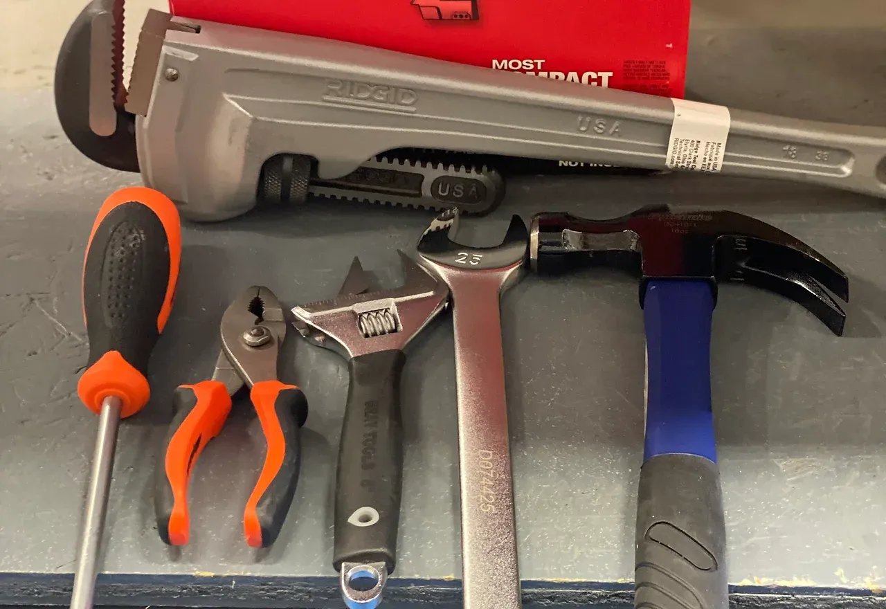 Tools including a pipe wrench, hammer, screwdriver, pliers, and adjustable wrench.