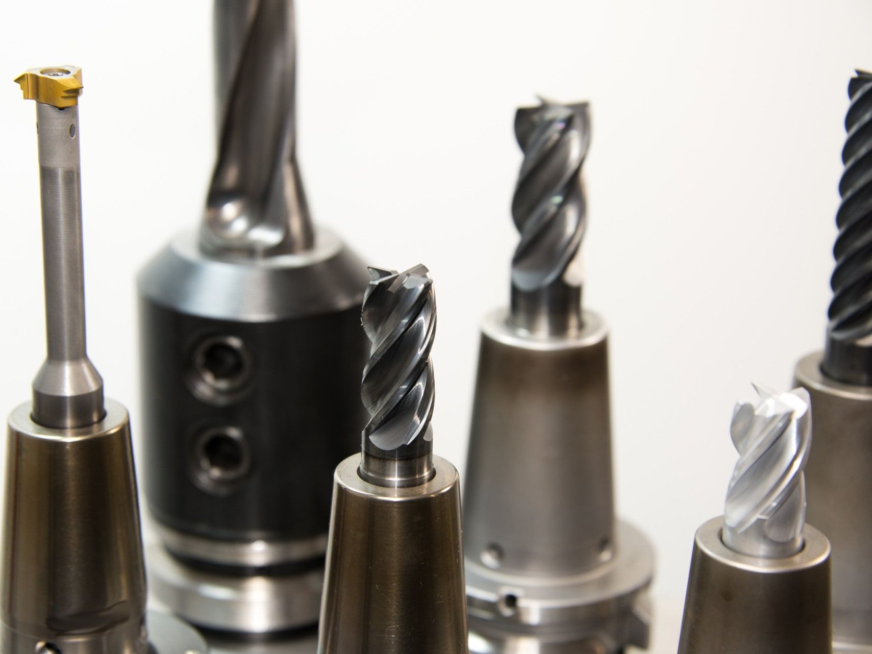Close-up of various metal drill bits with different cutting edges, in a manufacturing setting.