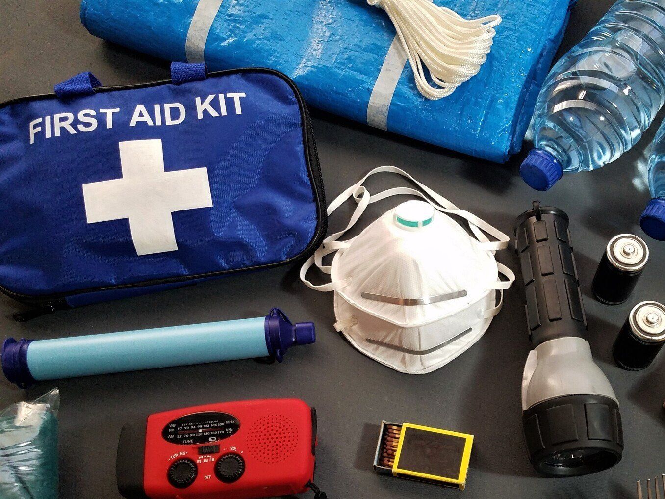 Emergency preparedness supplies: first aid kit, water bottles, flashlight, face mask, radio, water filter.