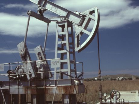 Oil pump jack extracting oil from a well, set against a blue sky and dry landscape.