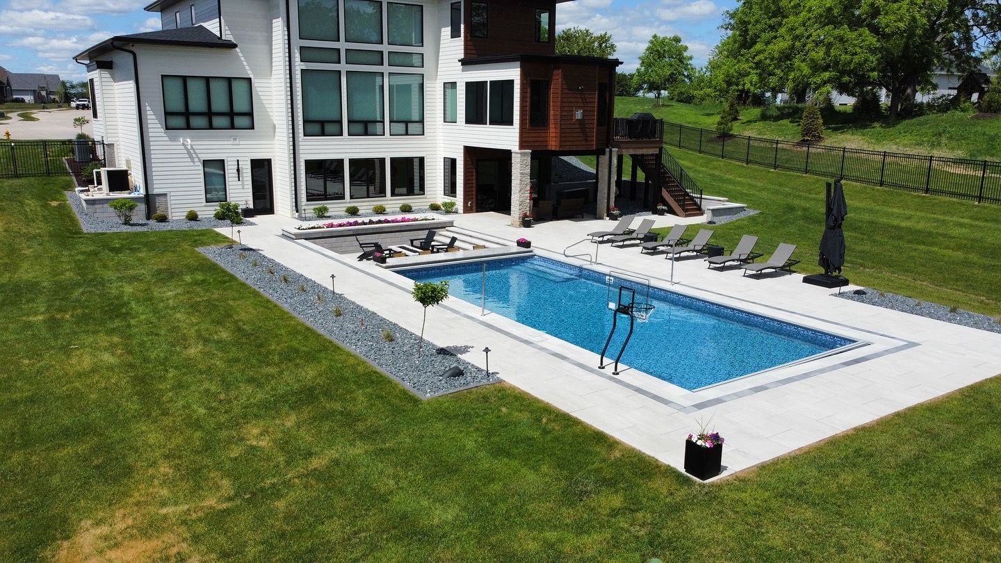 Aerial view of a white multi-story house with a backyard featuring a rectangular swimming pool surrounded by a patio.