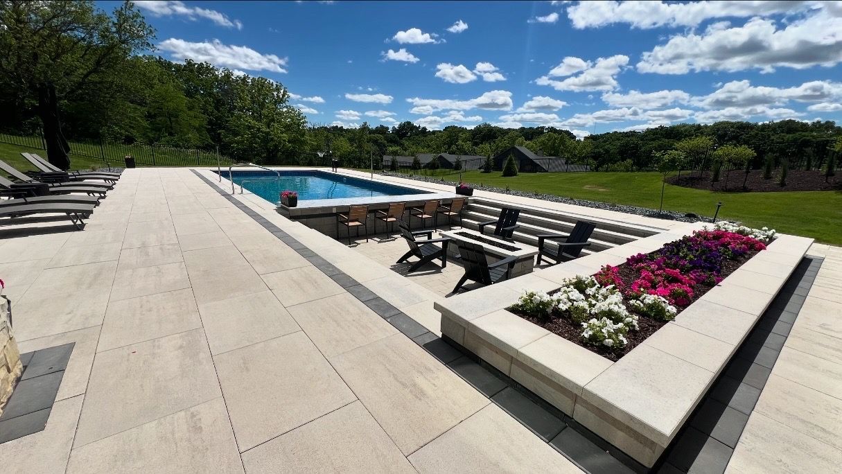 A sunken outdoor seating area with a fire pit beside a swimming pool, featuring stone pavers and a bed of flowers.