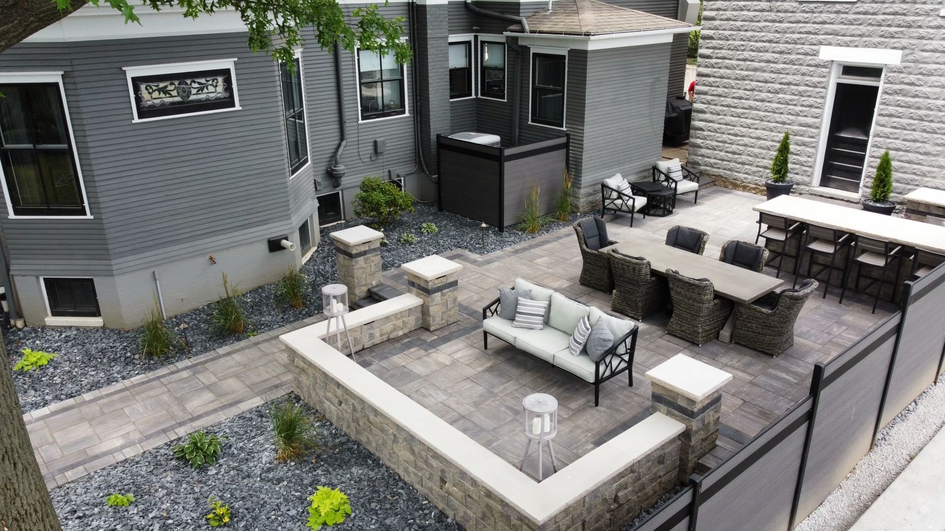 A gray house with a stone patio, outdoor seating, and a long dining table, surrounded by dark gravel landscaping.