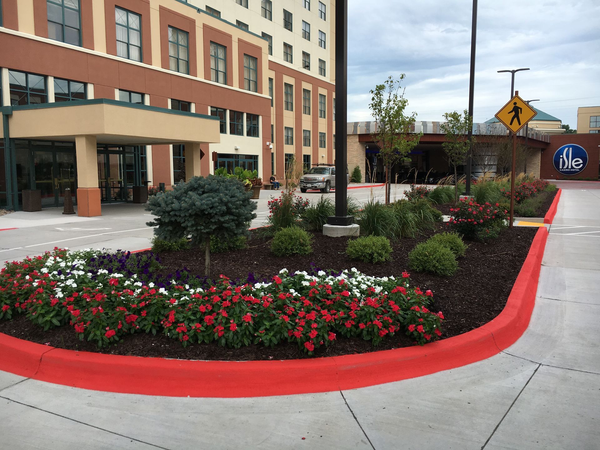 A landscaped traffic island with red-edged curbs, red flowers, and shrubs in front of a hotel entrance.