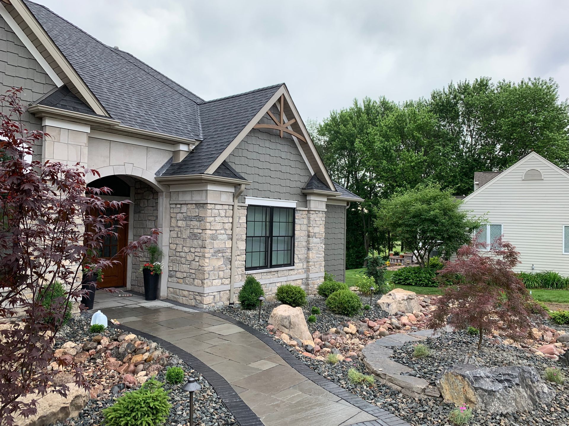 A stone and gray-sided house with a dark roof and arched entryway, featuring a landscaped front yard with gray gravel.