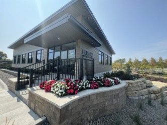 Modern one-story office building with a stone-walled planter filled with colorful flowers near the entrance.