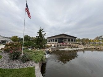 A pond with a small waterfall, landscaped rocks, and an American flag in front of a modern building under a cloudy sky.