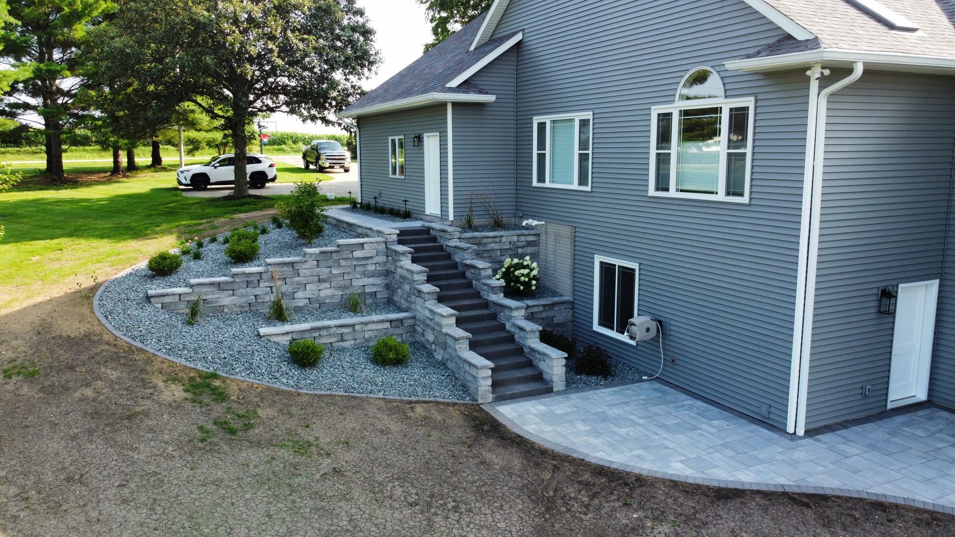 A grey house with stone retaining walls, matching stone stairs leading to a side door, and a stone patio.