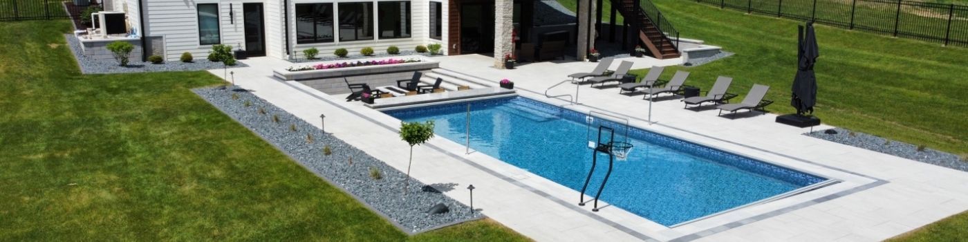An aerial view of a rectangular backyard pool with light blue water, a surrounding white deck, and lounge chairs.