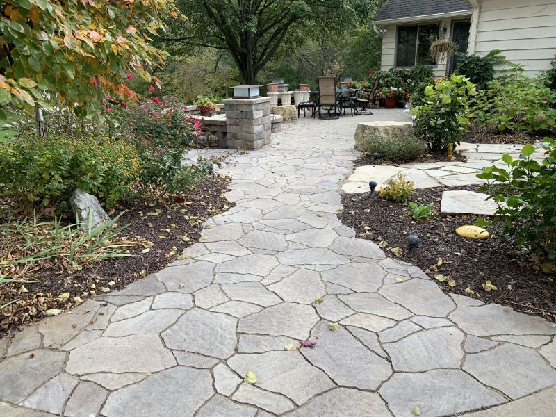 Stone pathway leads to a patio with outdoor furniture. Mulched flowerbeds border the path.