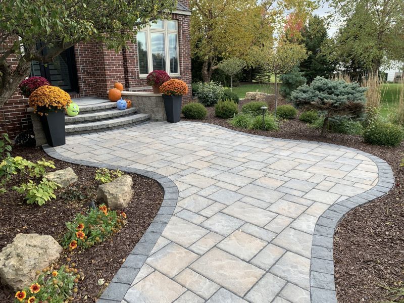 Brick home with a curving paver walkway. Mums in pots flank steps, a landscaped yard borders the path.